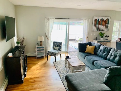 Cozy living room with a sectional sofa, chair, TV, and sliding doors leading to a deck by the water.