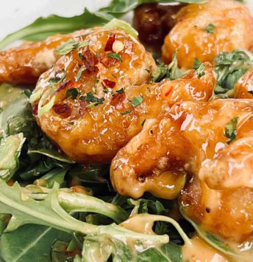 Close-up of crispy shrimp drizzled with sauce, served on a bed of fresh greens.