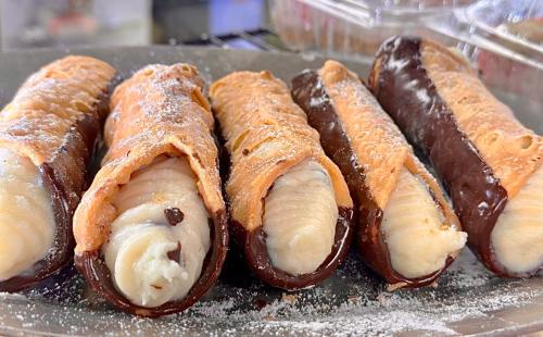 A close-up of four cannoli filled with creamy filling and dipped in chocolate, dusted with powdered sugar.