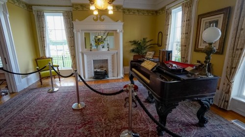 A vintage room featuring a piano, fireplace, and decorative furnishings, with a warm yellow wall and elegant curtains.