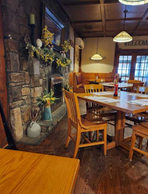 Cozy restaurant interior with wooden tables, chairs, and a stone fireplace decorated with flowers. Warm, inviting atmosphere.