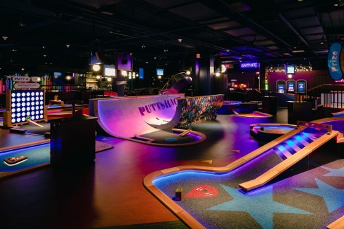 A vibrant indoor mini-golf course featuring colorful obstacles and neon lighting.