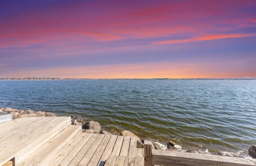 A serene lakeside view at sunset, featuring calm waters and a colorful sky with shades of purple and orange.