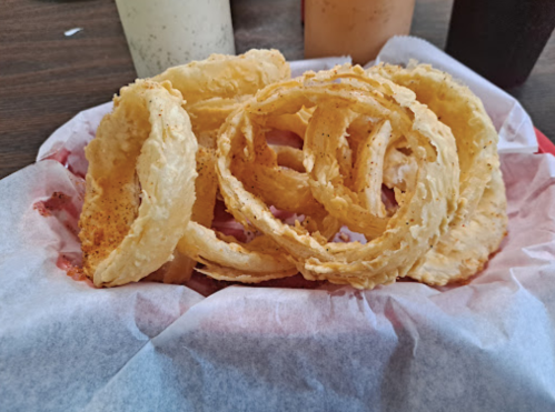 A plate of crispy onion rings served on parchment paper, with drinks in the background.
