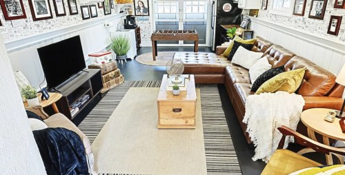 Cozy living room with a brown leather sofa, coffee table, TV, and decor, featuring a foosball table and plants.
