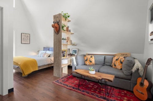 Cozy interior featuring a living area with a gray sofa, wooden coffee table, and a bedroom with a yellow blanket.