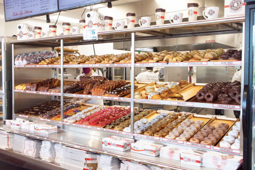 A display case filled with a variety of colorful donuts and pastries, neatly arranged on wooden trays.