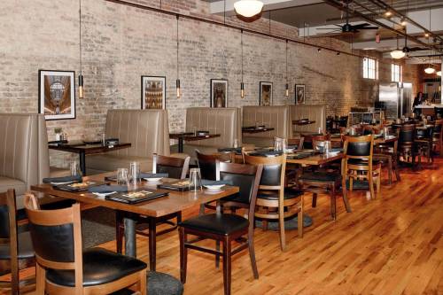 Interior of a modern restaurant featuring wooden floors, booth seating, and exposed brick walls.