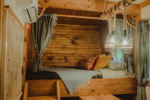 Cozy wooden loft bed with soft pillows, blankets, and decorative curtains in a warm, inviting space.