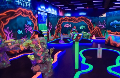 A vibrant glow-in-the-dark mini-golf course with colorful coral and fish designs.