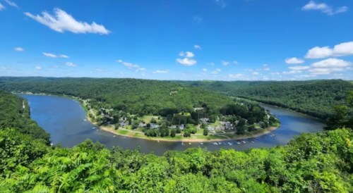 A scenic view of a river winding through lush green hills under a bright blue sky with scattered clouds.