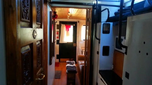 Interior view of a cozy cabin, featuring wooden doors, a small living area, and a staircase leading to upper bunks.