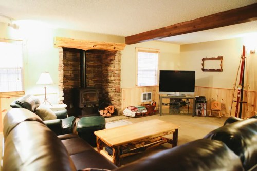 Cozy living room with a stone fireplace, wooden beams, a TV, and comfortable seating.