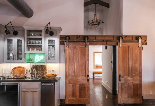 A modern kitchen with sliding barn doors, glass cabinets, and a cozy hallway leading to a well-lit room.