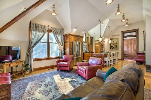 Cozy living room with red chairs, a brown sofa, wooden cabinetry, and a dining area, featuring large windows and warm lighting.