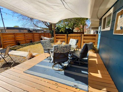 A cozy outdoor patio with a table and chairs, surrounded by wooden fencing and a sunny blue sky.