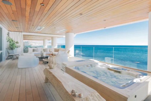 Luxurious outdoor space with a hot tub, wooden flooring, and stunning ocean views. Bright and inviting atmosphere.