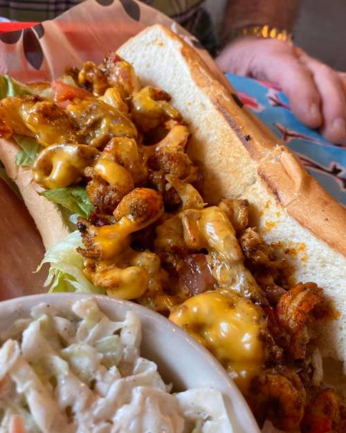 A close-up of a shrimp sandwich with lettuce, tomatoes, and melted cheese, served with a side of coleslaw.
