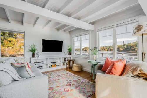 Cozy living room with large windows, a TV, colorful pillows, and a patterned rug, overlooking a scenic view.