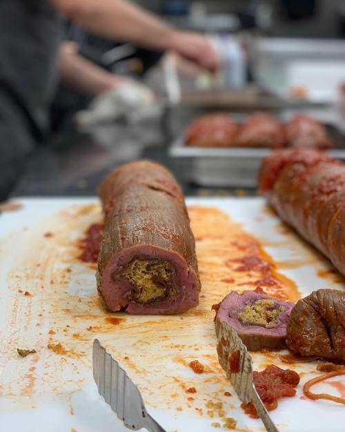 A sliced meat roll with stuffing, resting on a cutting board with sauce, in a kitchen setting.