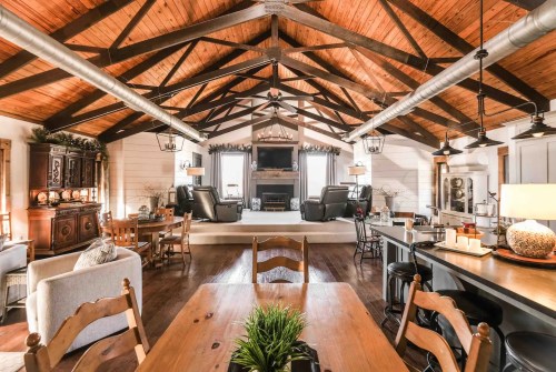 Spacious living area with wooden beams, cozy seating, and a dining table, featuring warm, rustic decor.