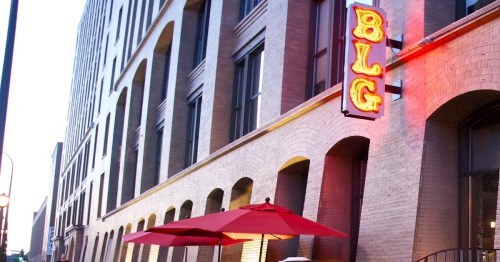 A building exterior with a neon sign reading "BLG" and a red umbrella on a patio.