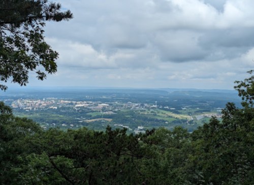 A panoramic view of a valley with a town, surrounded by green trees and cloudy skies.
