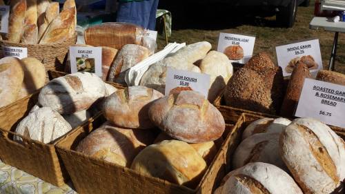 A variety of artisanal breads displayed in baskets at a market, with price signs for each type.