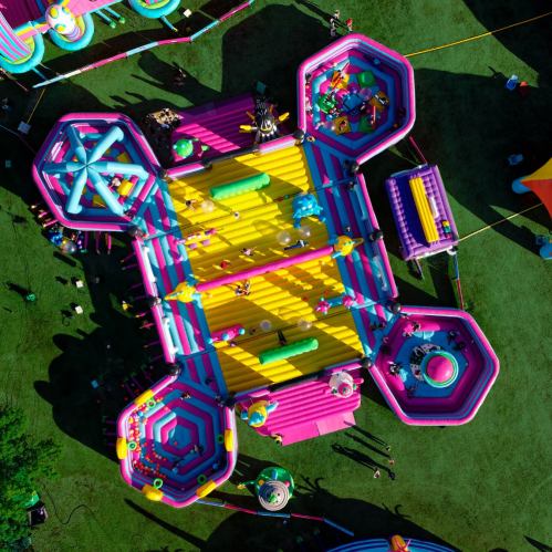 Aerial view of colorful inflatable play structures and children playing on a sunny day in a grassy area.