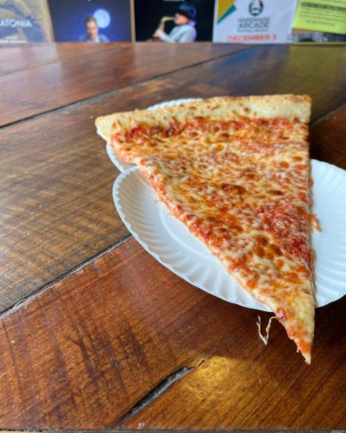A slice of cheese pizza on a paper plate, resting on a wooden table.