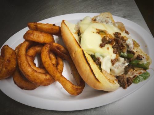 A plate featuring a loaded sandwich with beef, peppers, and cheese, alongside crispy curly fries.