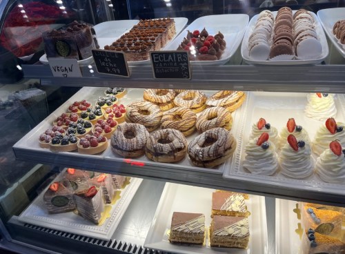 A display case filled with various pastries, including eclairs, donuts, and cakes, some decorated with fruit.