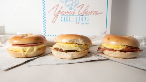 Three bagels with various fillings: one with ham and egg, one with sausage and egg, and one with bacon and egg, displayed with a logo.