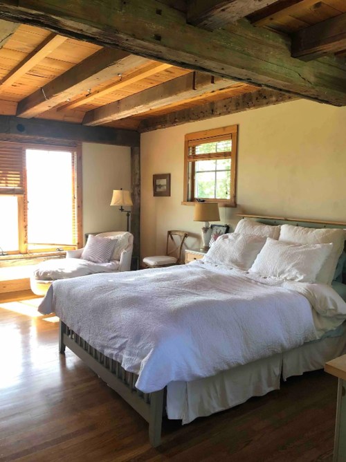 Cozy bedroom with a wooden ceiling, a large bed, and a sunny window with a seating area.