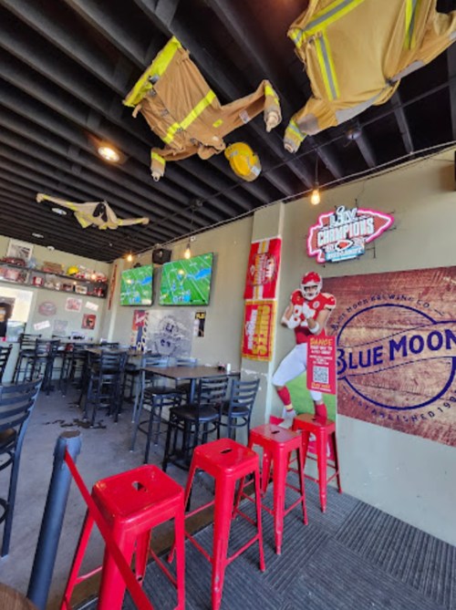 Interior of a sports bar with red stools, TVs showing a game, and firefighter gear hanging from the ceiling.