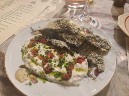 A plate with crispy fish skin and a creamy dip topped with sun-dried tomatoes and herbs, set on a decorative dish.