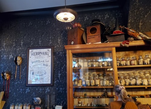 A cozy room with dark wallpaper, a glass cabinet filled with jars, and eclectic decor, including masks and instruments.