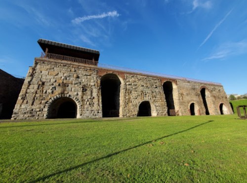Historic stone structure with arched openings, set against a clear blue sky and green grass.