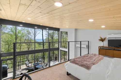 Bright, modern bedroom with large windows overlooking trees and a scenic view, featuring a cozy bed and stylish decor.
