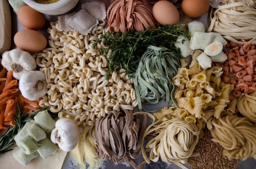 An assortment of fresh pasta, eggs, garlic, herbs, and other ingredients arranged on a surface.