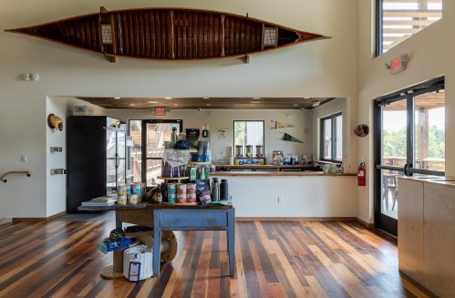 Interior of a rustic space with wooden floors, a canoe hanging from the ceiling, and a counter with various items.