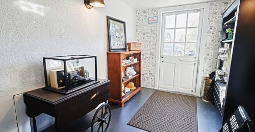 A cozy entryway featuring a display case, wooden shelves, and a door leading outside, with patterned wallpaper.
