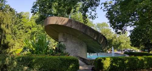 A unique, curved structure surrounded by lush greenery and a tranquil pool, creating a serene outdoor setting.