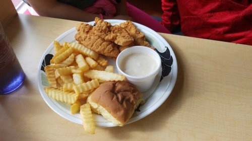 A plate with crispy chicken tenders, crinkle-cut fries, a small bun, and a cup of dipping sauce.