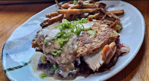 A plate of fried chicken topped with gravy and green onions, served with a side of crispy French fries.