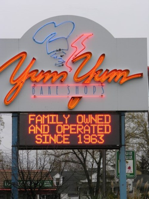 Sign for Yum Yum Bake Shops, featuring neon lettering and a message about being family-owned since 1963.