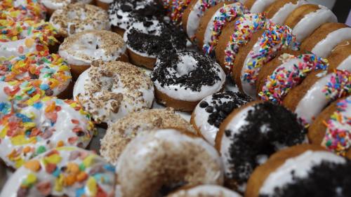 A colorful assortment of donuts topped with sprinkles, crushed cookies, and cereal, arranged neatly on a tray.
