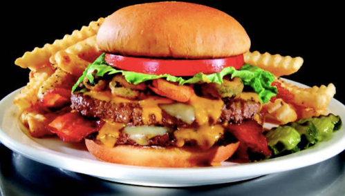A juicy cheeseburger with lettuce, tomato, and pickles, served with crinkle-cut fries on a white plate.