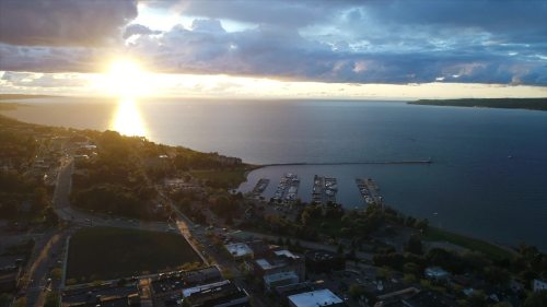 Aerial view of a serene lake at sunset, with boats docked and clouds reflecting golden light on the water.