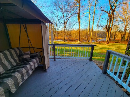 A cozy porch with a striped sofa overlooks a serene river and trees in the background under a clear blue sky.